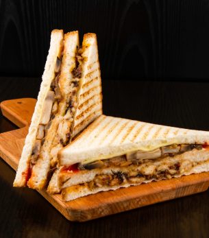 Grilled Chicken Club Sandwich with Mushrooms and Cheese isolated on wooden board side view of fast food on dark background Grilled Chicken Club Sandwich with Mushrooms and Cheese isolated on wooden board side view of fast food on dark background