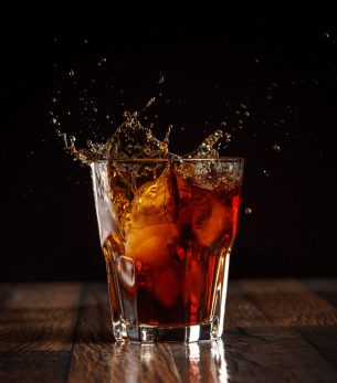 Splash in glass of cola with ice on gray gradient background Splash in glass of cola with ice on gray gradient background